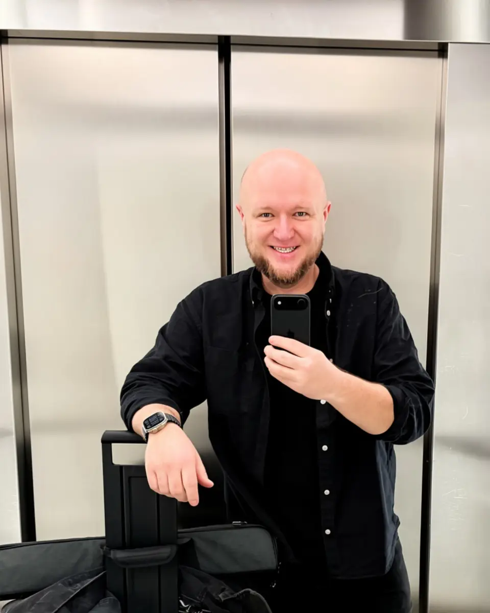 Michał Liszcz, założyciel Motion Pikczer, trzyma smartfon w dłoni, czarna koszula, uśmiech, nowoczesne wnętrze biurowe z szkłem matowym.