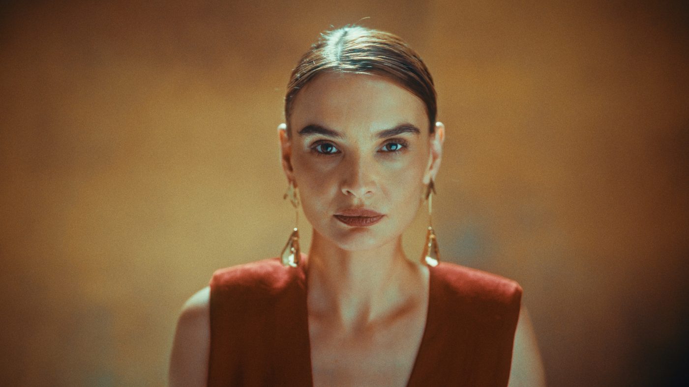 Produkcja filmów reklamowych Kraków | Motion Pikczer B2B 3 Kobieta w czerwonym żakiecie, perłowe kolczyki, złote oświetlenie studyjne. Kampania premium B2B.