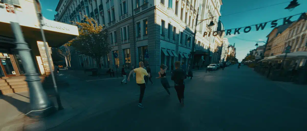 Film promujący wydarzenie Igrzyska Wolności 3 Biegacze na ulicy Piotrkowskiej w Łodzi, architektura kamienic, światło słoneczne, produkcja filmu.