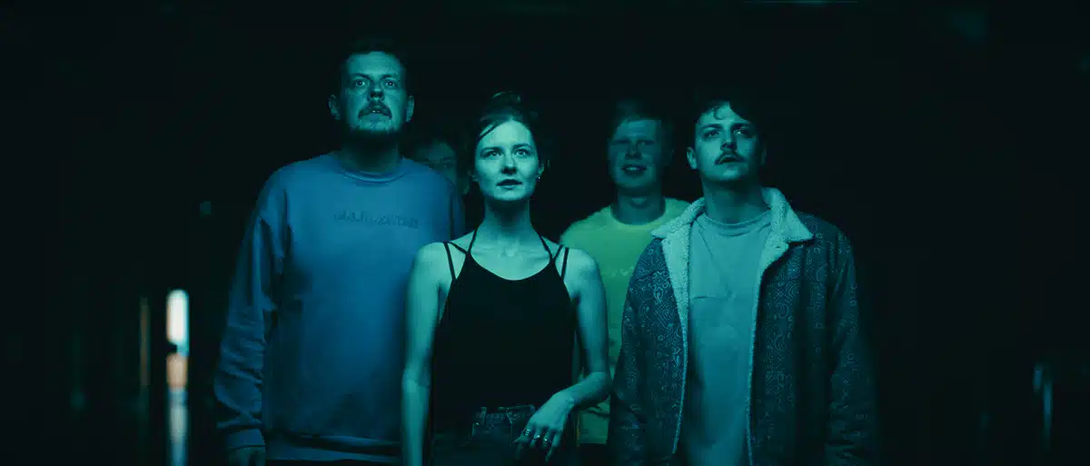 Film promujący wydarzenie Igrzyska Wolności 6 Czterech aktorów w ciemnym wnętrzu, oświetlenie turkusowe, napięta atmosfera, produkcja filmowa Motion Pikczer.