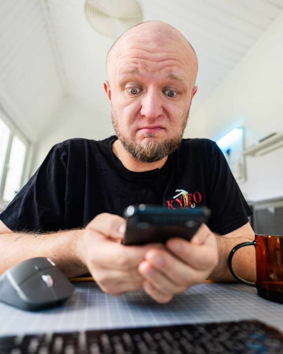 Menedżer zaskoczony treścią smartfona przy biurku z klawiaturą i myszą — reakcja na zmiany regulacyjne AI