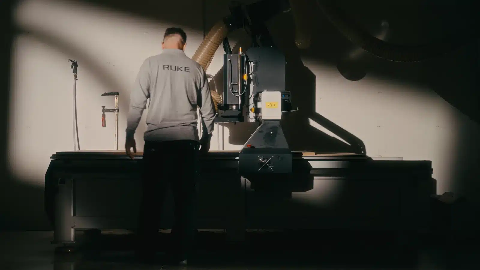 Elementy wizualnej narracji marki premium na Instagramie 2 Pracownik przy maszynie CNC w pojedynczym snopie bocznego światła, reszta kadru w cieniu